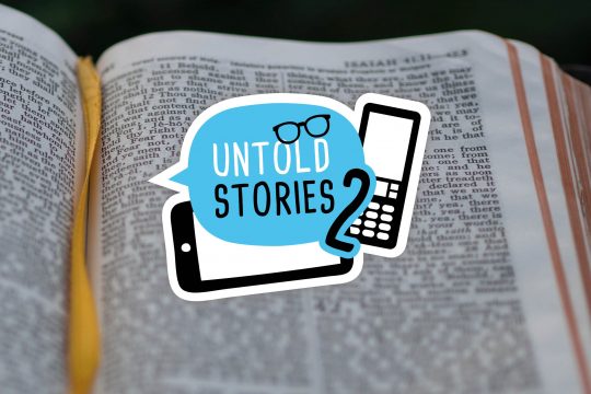 Bild mit Untold Stories Logo (Grafik mit Sprechblase mit dem Schriftzug "Untold Stories 2" und zwei Smartphones) über aufgeschlagener Bibel.